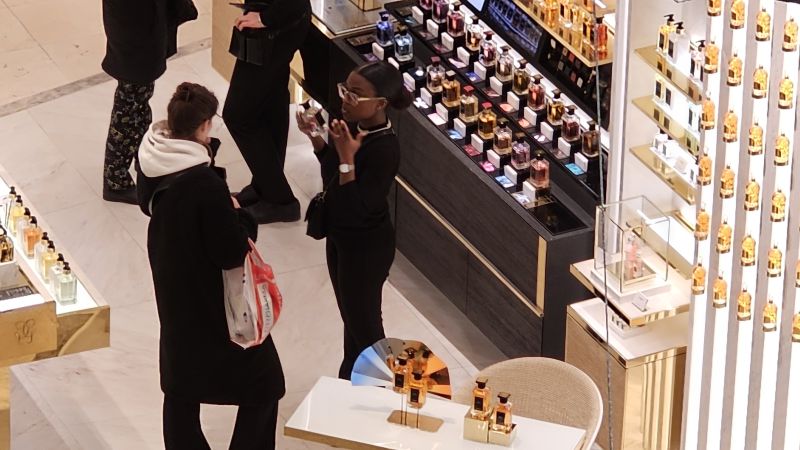 Sales associate and customer talking at a luxury perfume counter, testing a scent—human connection and attentive service, not a scripted transaction.